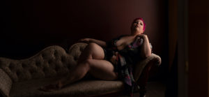 Beautiful boudoir photo of plus-size woman with pink hair swooning on an antique couch