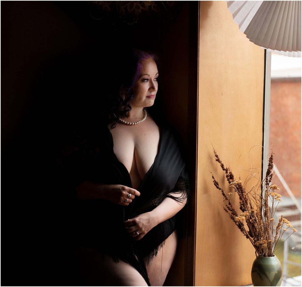 Softly lit photo of a woman in a black shawl standing by a window