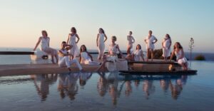 Group boudoir photo from a women's retreatof women wearing white by an infintity pool at sunset in Greece